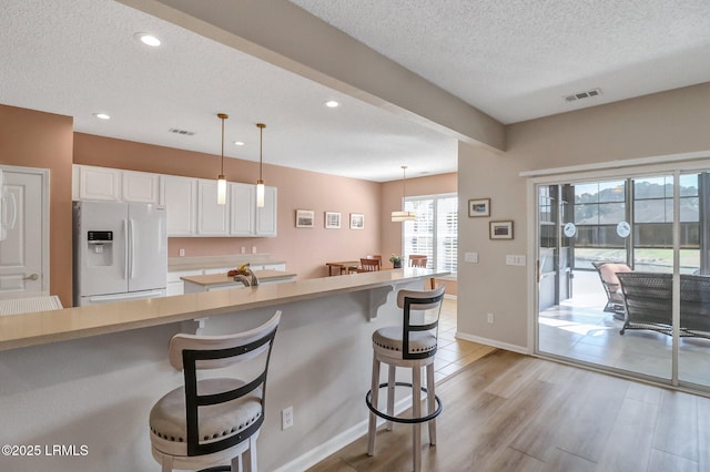 kitchen featuring visible vents, light wood-style flooring, white cabinetry, white fridge with ice dispenser, and a kitchen bar