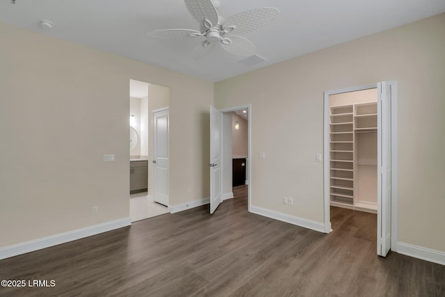 unfurnished bedroom with connected bathroom, a walk in closet, dark hardwood / wood-style floors, a closet, and ceiling fan