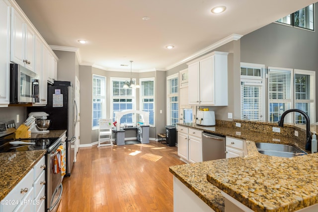 kitchen with sink, dark stone countertops, white cabinets, hanging light fixtures, and stainless steel appliances