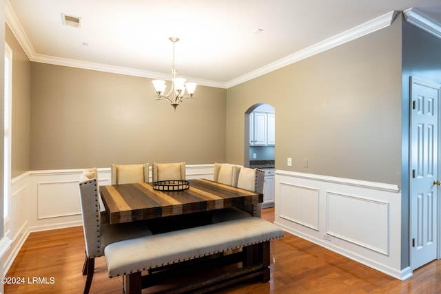 dining area with hardwood / wood-style flooring, ornamental molding, and a notable chandelier