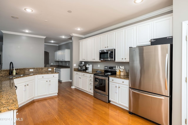 kitchen with sink, dark stone countertops, light wood-type flooring, stainless steel appliances, and white cabinets