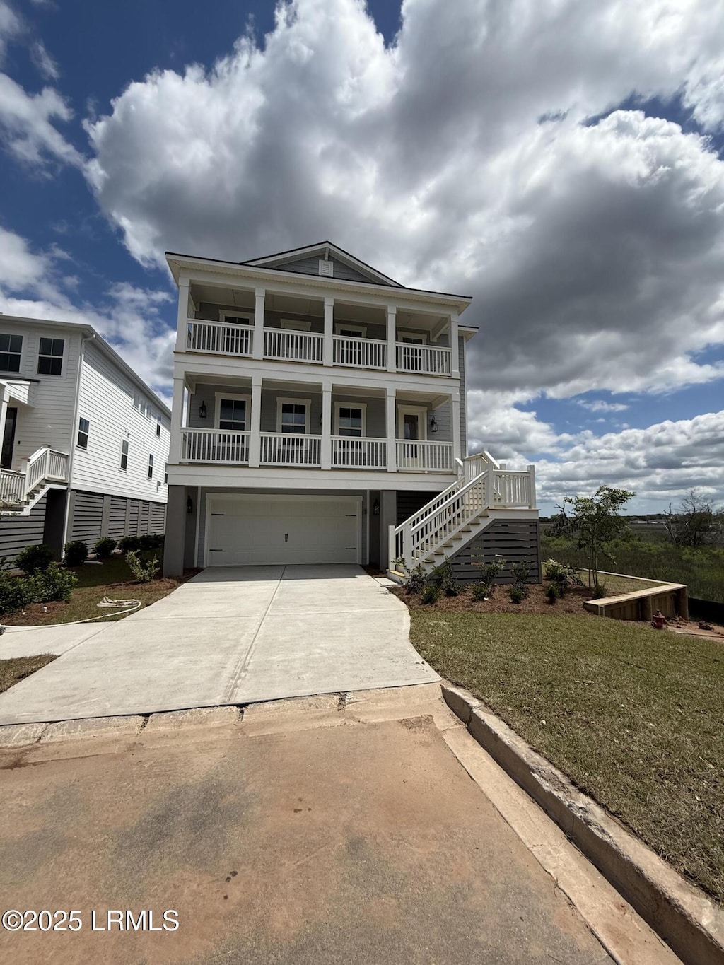 raised beach house with stairs, a balcony, driveway, and an attached garage