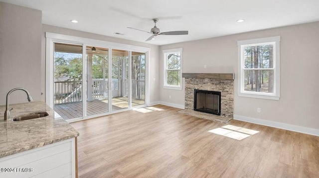 unfurnished living room featuring ceiling fan, sink, a fireplace, and light hardwood / wood-style flooring