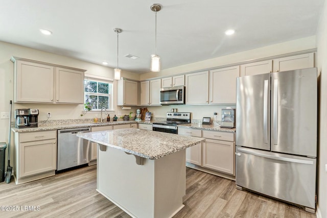 kitchen featuring a kitchen island, appliances with stainless steel finishes, light stone countertops, light wood-type flooring, and a sink