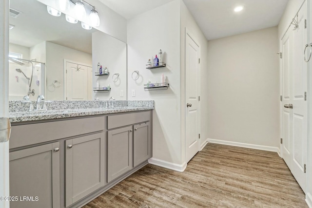 full bathroom with double vanity, baseboards, a sink, and wood finished floors