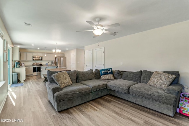 living area with light wood-type flooring, recessed lighting, visible vents, and ceiling fan with notable chandelier