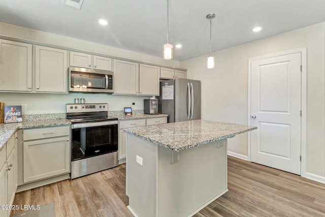 kitchen featuring light wood-type flooring, light stone counters, stainless steel appliances, and decorative light fixtures