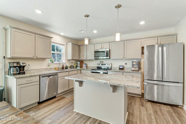 kitchen with light stone counters, light wood-style flooring, appliances with stainless steel finishes, a center island, and pendant lighting