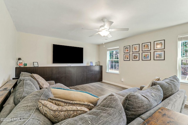 living area with a wealth of natural light, baseboards, ceiling fan, and light wood finished floors