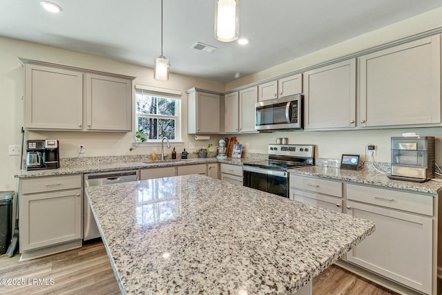 kitchen featuring stainless steel appliances, a sink, visible vents, hanging light fixtures, and light wood finished floors