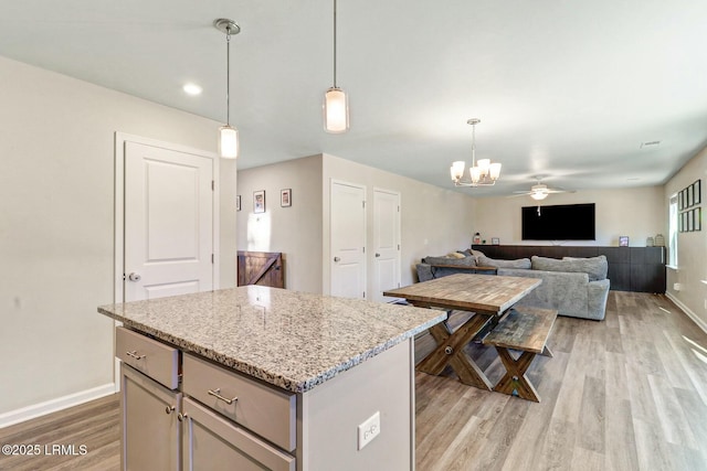 kitchen featuring a kitchen island, open floor plan, light wood-type flooring, light stone countertops, and pendant lighting