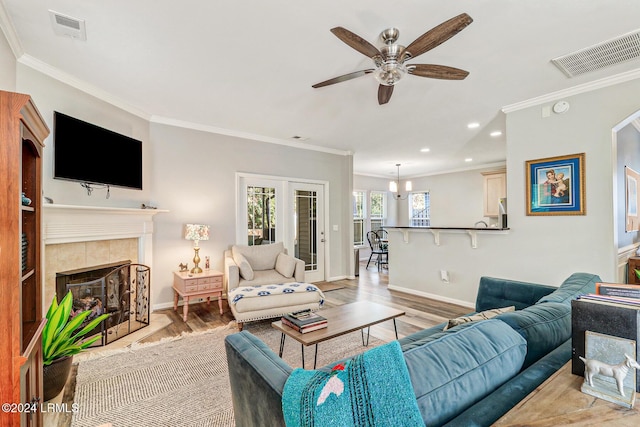 living room featuring hardwood / wood-style flooring, ornamental molding, and a tile fireplace