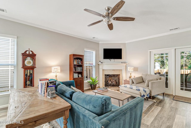 living room with a tile fireplace, ornamental molding, ceiling fan, and light wood-type flooring