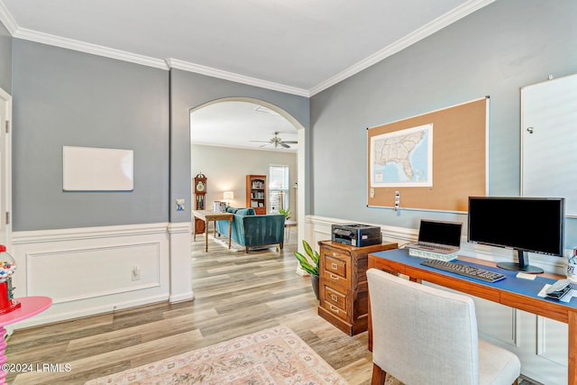 office featuring crown molding, light wood-type flooring, ceiling fan, arched walkways, and a wainscoted wall