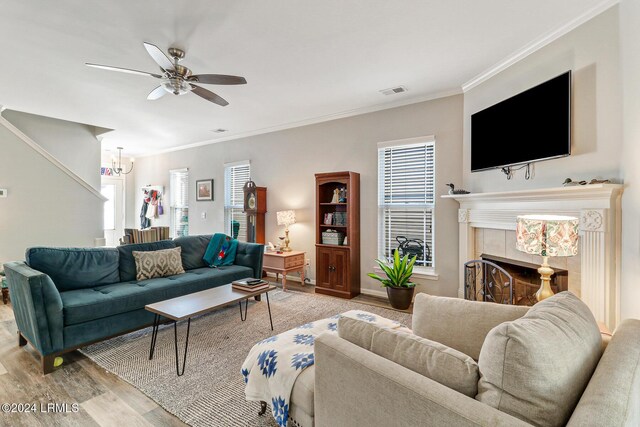 living room featuring crown molding, ceiling fan with notable chandelier, a tile fireplace, and light hardwood / wood-style flooring