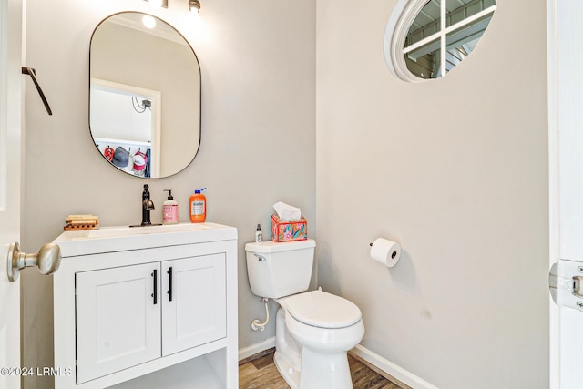 half bathroom with toilet, vanity, wood finished floors, and baseboards