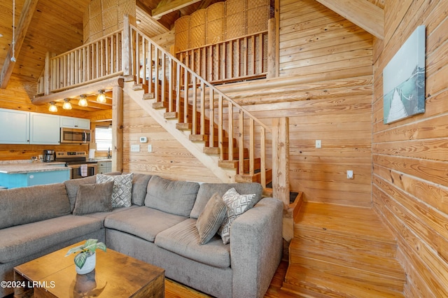 living room with beam ceiling, wooden walls, high vaulted ceiling, wooden ceiling, and light wood-type flooring