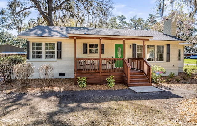 view of front of property featuring crawl space, brick siding, a chimney, and covered porch