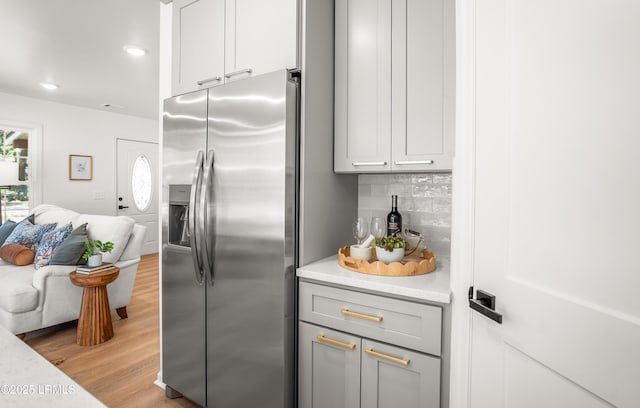 kitchen featuring stainless steel fridge, open floor plan, light countertops, light wood-type flooring, and backsplash