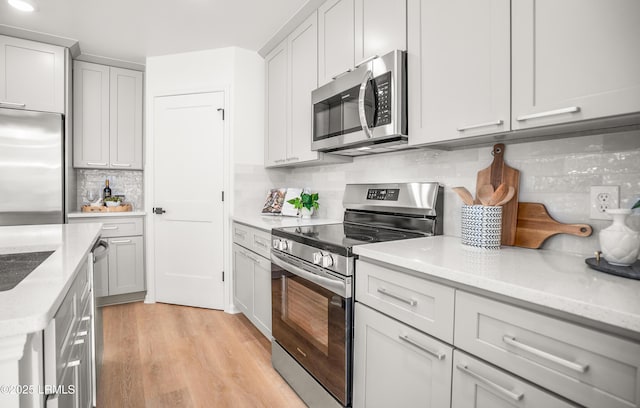 kitchen with light stone countertops, light wood-style flooring, appliances with stainless steel finishes, and tasteful backsplash