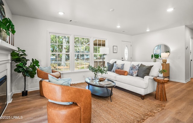 living area with light wood-type flooring, a glass covered fireplace, visible vents, and recessed lighting