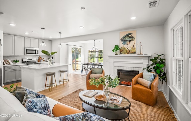 living area with recessed lighting, visible vents, light wood-style flooring, a brick fireplace, and baseboards