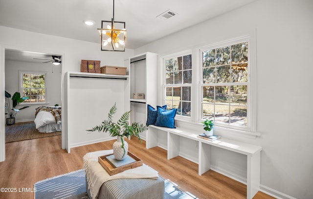 living area with light wood-type flooring, visible vents, baseboards, and ceiling fan with notable chandelier