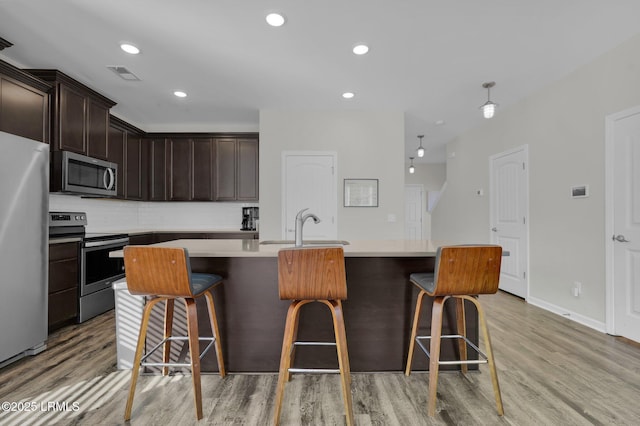 kitchen with a breakfast bar, sink, appliances with stainless steel finishes, a kitchen island with sink, and decorative backsplash