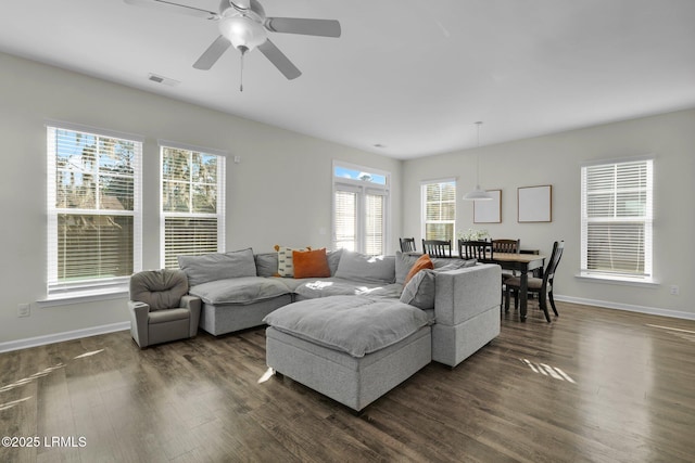 living room with a wealth of natural light, dark wood-type flooring, and ceiling fan