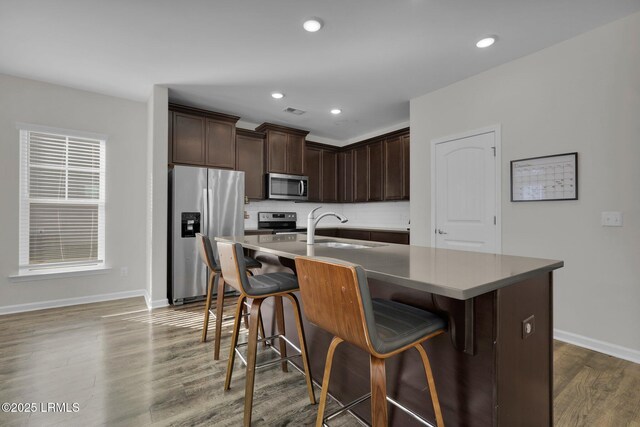 kitchen featuring a breakfast bar, sink, a kitchen island with sink, dark brown cabinetry, and stainless steel appliances