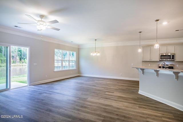 unfurnished living room featuring ceiling fan with notable chandelier, ornamental molding, and dark hardwood / wood-style floors