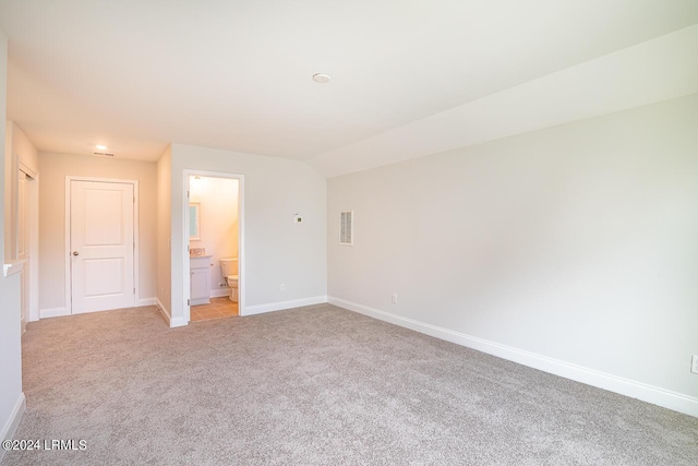 unfurnished bedroom featuring ensuite bathroom, lofted ceiling, and light carpet