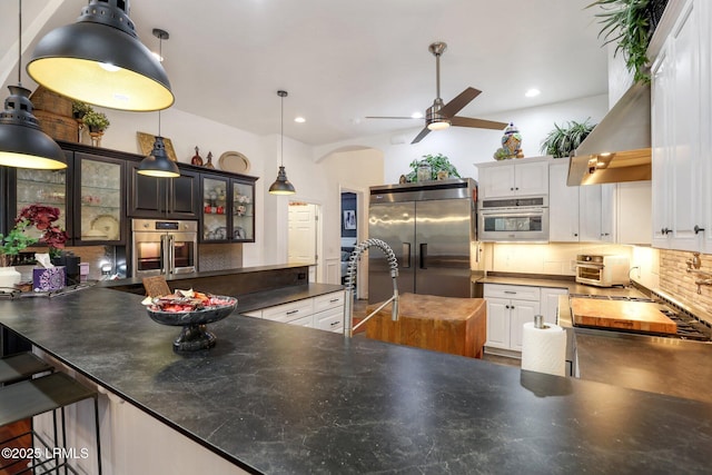 kitchen featuring pendant lighting, wall chimney range hood, appliances with stainless steel finishes, white cabinetry, and tasteful backsplash