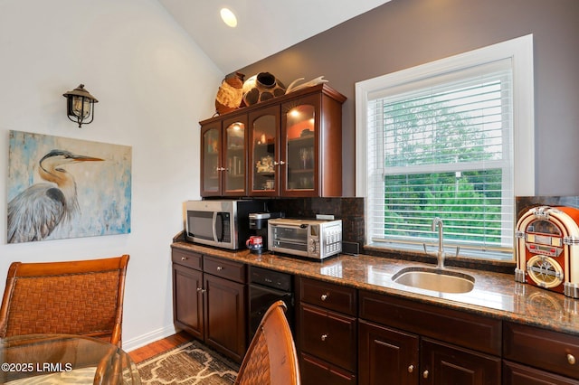 kitchen with sink, vaulted ceiling, dark brown cabinets, light hardwood / wood-style flooring, and dark stone counters