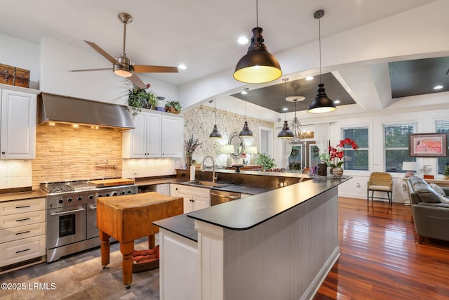 kitchen featuring decorative light fixtures, white cabinetry, sink, stainless steel appliances, and wall chimney range hood