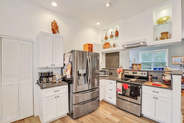 kitchen featuring appliances with stainless steel finishes, white cabinetry, range hood, light hardwood / wood-style floors, and dark stone counters