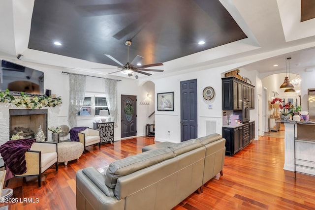 living room featuring ceiling fan, light hardwood / wood-style floors, and a tray ceiling