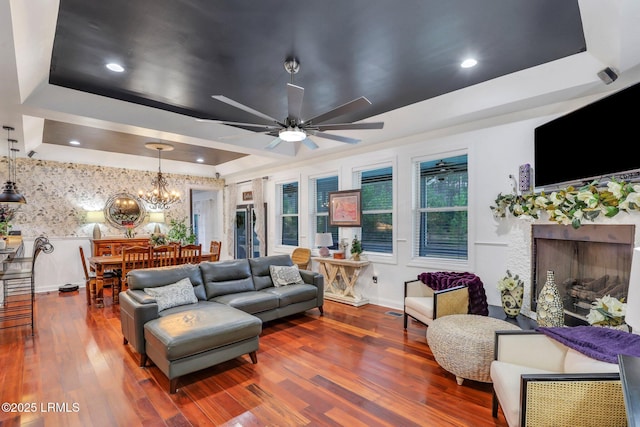 living room with ceiling fan with notable chandelier, a premium fireplace, a raised ceiling, and hardwood / wood-style floors