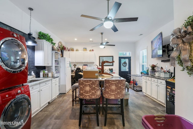 kitchen featuring a breakfast bar area, dark hardwood / wood-style floors, stacked washer / drying machine, an island with sink, and white cabinets