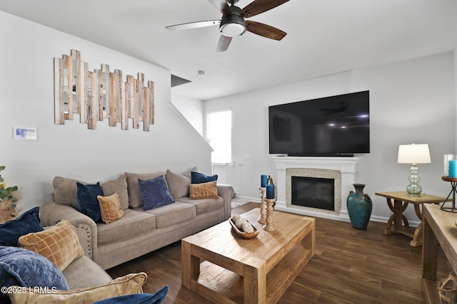 living room with a stone fireplace, baseboards, a ceiling fan, and dark wood finished floors