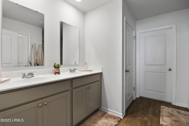 full bath with double vanity, baseboards, a sink, and wood finished floors