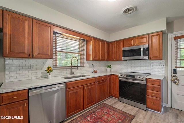 kitchen featuring appliances with stainless steel finishes, a sink, light countertops, light wood finished floors, and tasteful backsplash