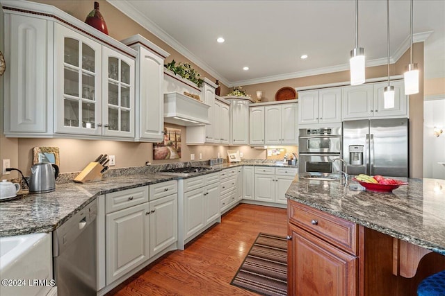 kitchen with wood-type flooring, appliances with stainless steel finishes, pendant lighting, dark stone counters, and white cabinets