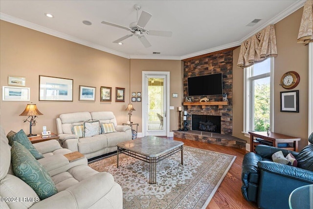 living room featuring hardwood / wood-style flooring, crown molding, plenty of natural light, and a stone fireplace