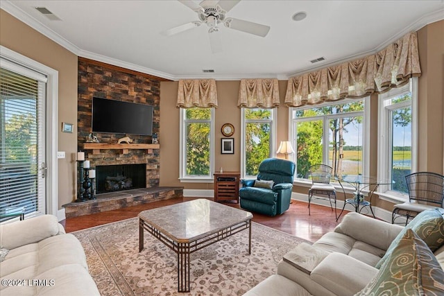 living room with wood-type flooring, a stone fireplace, ornamental molding, and ceiling fan