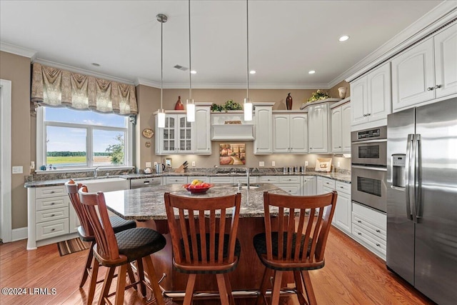 kitchen with pendant lighting, white cabinets, a kitchen bar, a kitchen island with sink, and stainless steel appliances