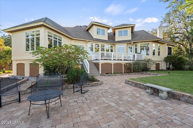 rear view of property featuring a wooden deck, a lawn, and a patio