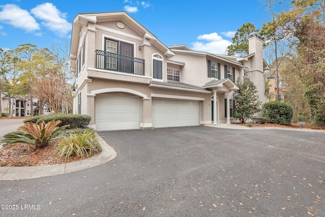 view of front of home with an attached garage, driveway, a chimney, and stucco siding