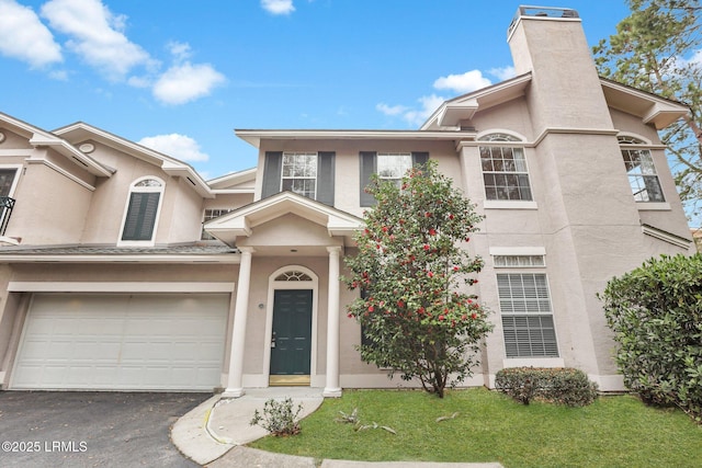 view of property with a garage, a chimney, aphalt driveway, a front lawn, and stucco siding