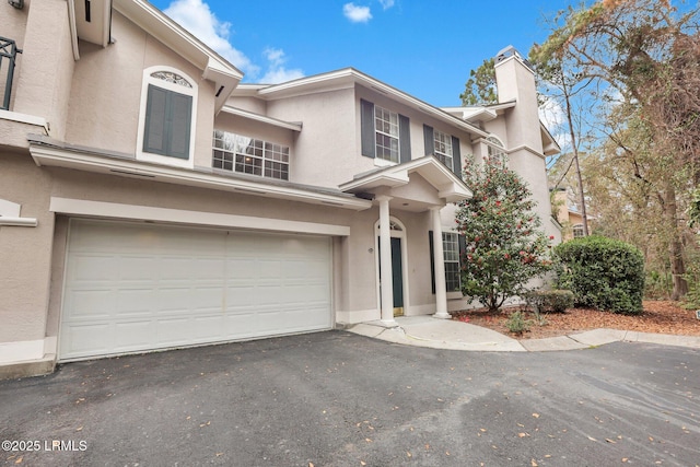 view of front of home featuring a garage, aphalt driveway, a chimney, and stucco siding